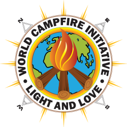 Home 12 | Galactic Federation of Light | The Campfire Circle Circular emblem logo for the World Campfire Initiative and The Campfire Circle founded by Trevor One Feather (Trevor Reichert) featuring three wooden logs arranged beneath a bright orange-gold flame, subtly forming a peace-sign shape within a circular sun-ring over a blue and green Earth globe. The globe is encircled by a golden ring and a white outer band with bold black lettering reading “WORLD CAMPFIRE INITIATIVE” at the top and “THE CAMPFIRE CIRCLE” at the bottom. Golden sunburst rays extend outward from behind the circle, symbolizing radiance, unity, and global coherence. Subtle directional markers (N, E, S, W) appear around the outer edge, reinforcing worldwide scope and a unified global mass meditation field.